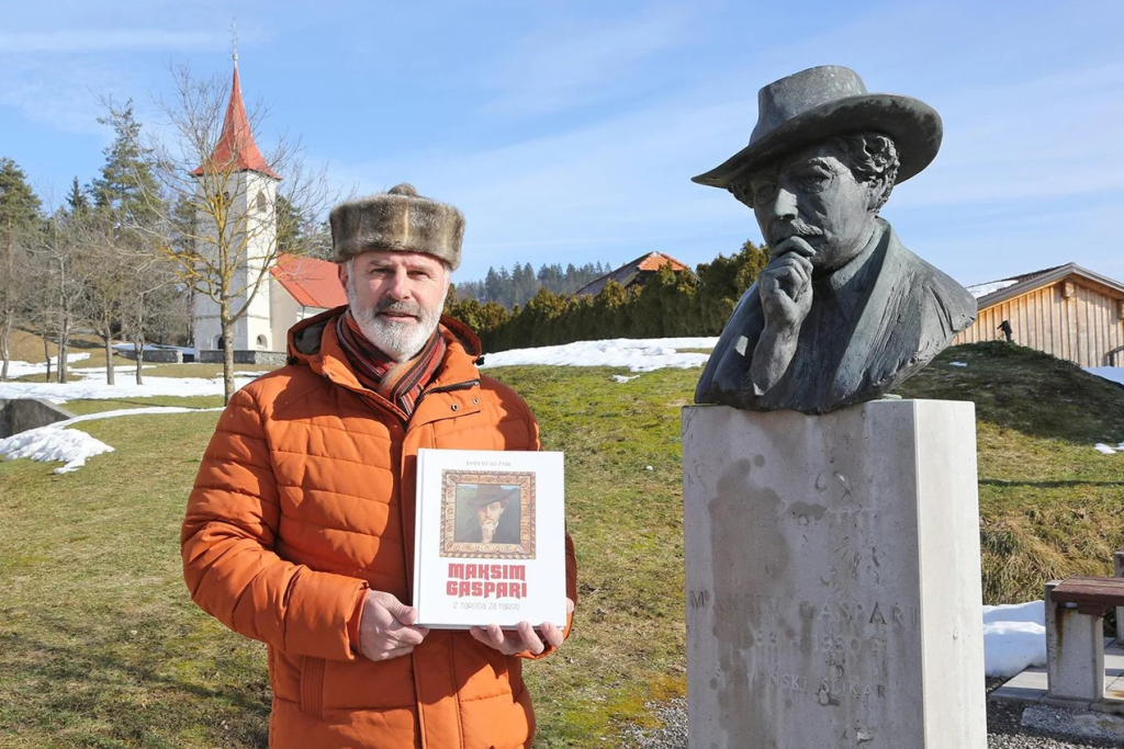Robert Kužnik z monografijo Maksim gaspari: iz naroda za narod stoji ob doprsnem spomeniku kipu slikarja.